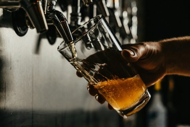 Bartender's hand is pouring brown liquid into clear drinking glass